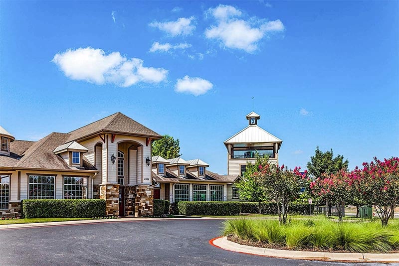 A clubhouse building rises above a rounded driveway in Manor Texas