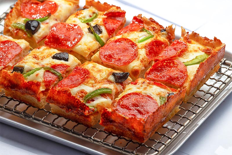 A sliced Detroit-style pizza sitting on a cooling tray