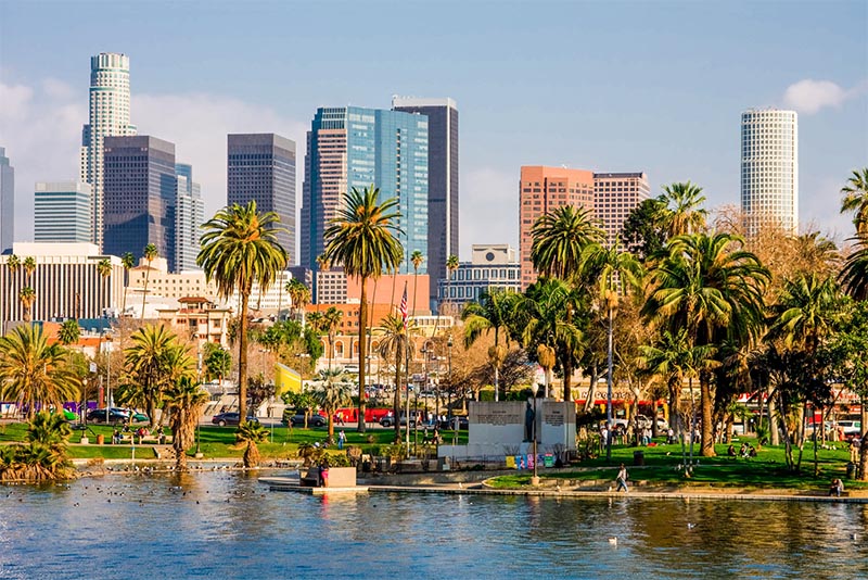 A pond in a park in Los Angeles with the Downtown skyline looming behind palm trees