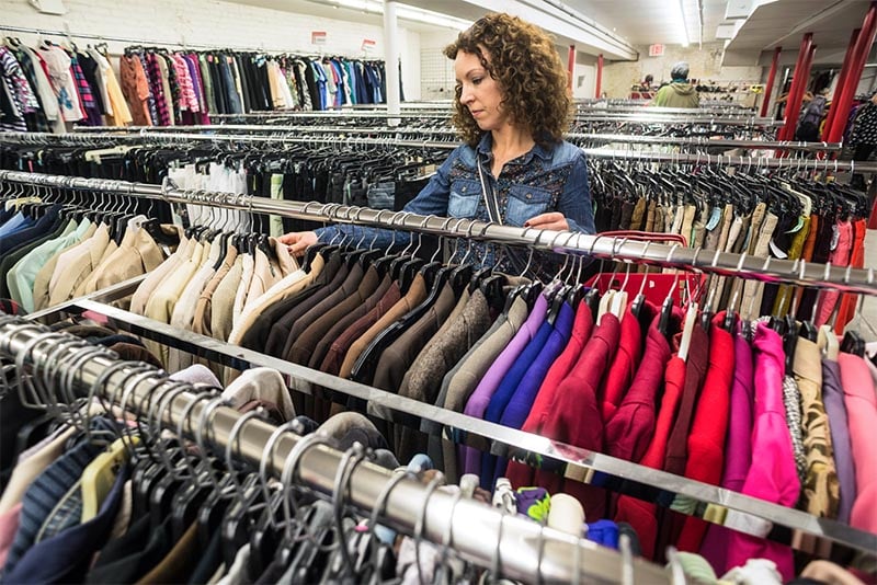 A woman sifting through clothing racks at a thrift shop