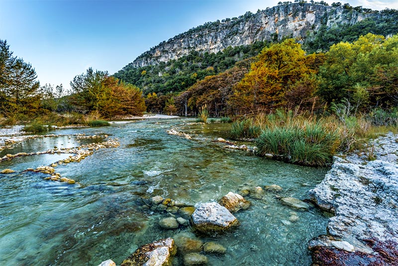 A river running over rocks with a large cliff behind it in Texas