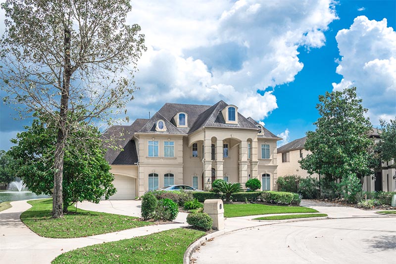 A luxury home with a large driveway and a pond behind it in Texas