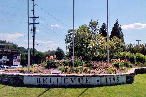 Sign for city of Bellevue, TN founded in 1794, with flag poles and flowerrs surrounding.
