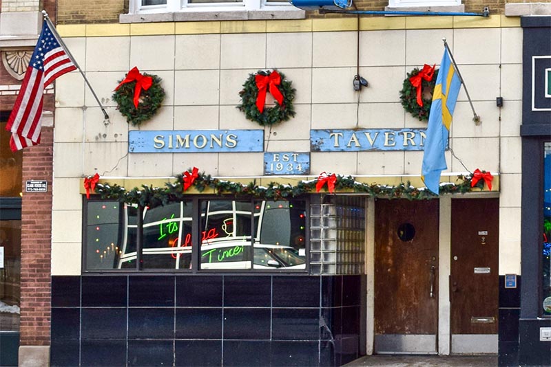 The outside facade of Simon's Tavern in Chicago with its blue sign and Christmas decor