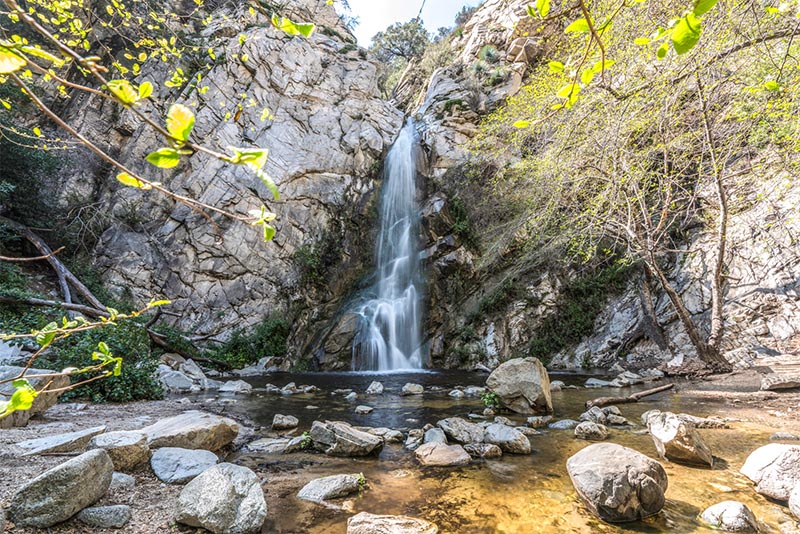 A landscape image of a tall waterfall falling into a basin and splashing over rocks