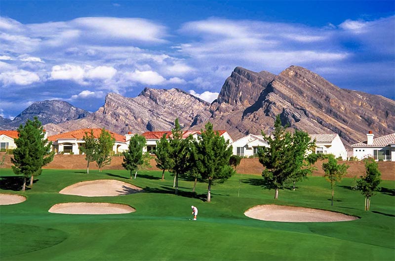 A man plays golf on a golf course with a large mountain behind him