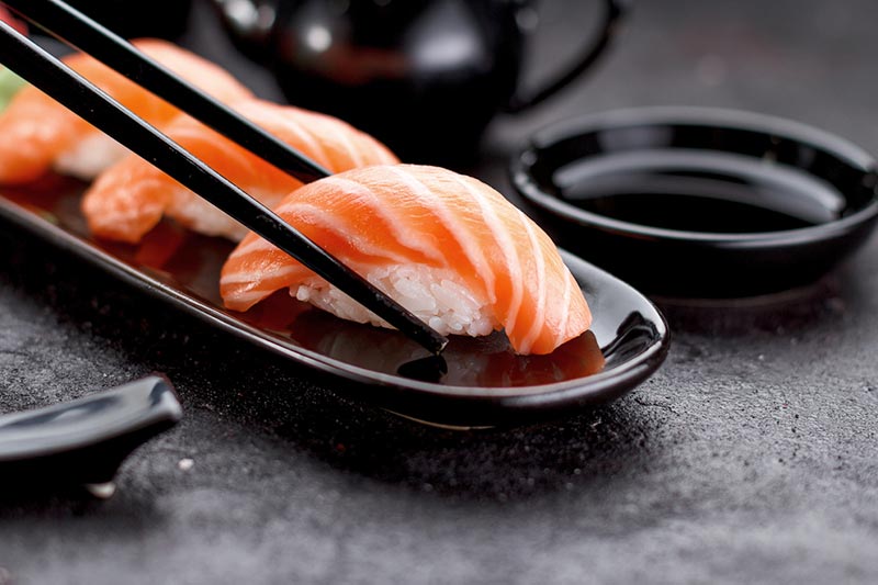 Salmon sushi nigiri on a black plate with chopsticks