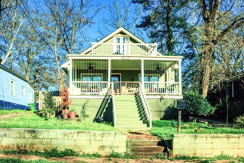 Exterior of colorful green home with patio.