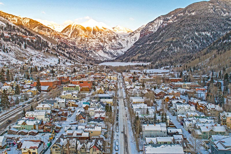 Aerial view of a small Colorado town with mountains in the background blanketed in snow