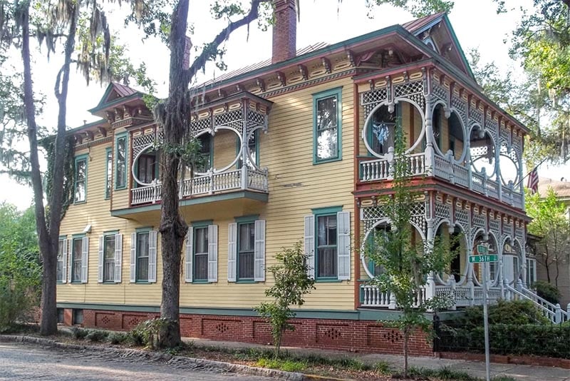 A historic home in Thomas Square in Savannah with yellow paneling, green windows, and intricate balconies