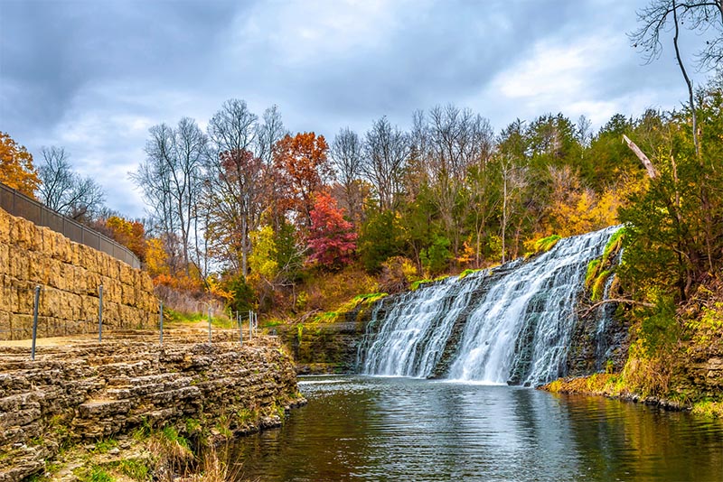 A large waterfall runs over a rock wall with fall foliage outside Chicago