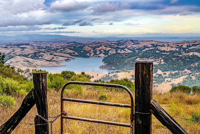 A gate along a hiking trail overlooks hills and fields in San Francisco
