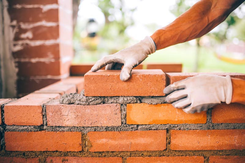 Two hands laying brick in front of window