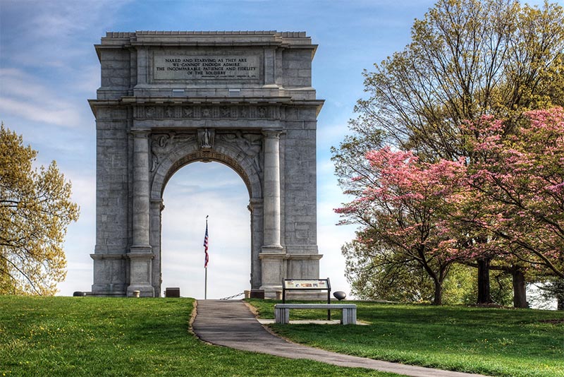 A large arched monument rises above the trail at Valley Forge National Historical Park in Philadelphia