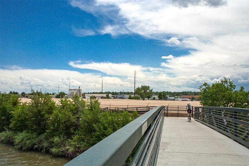 A person bikes up a bike path with some flat scenery behind them in Denver CO