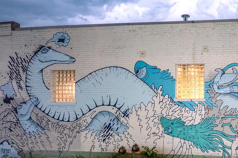 A mural of blue water dragons on a white brick wall in Hale Denver Colorado