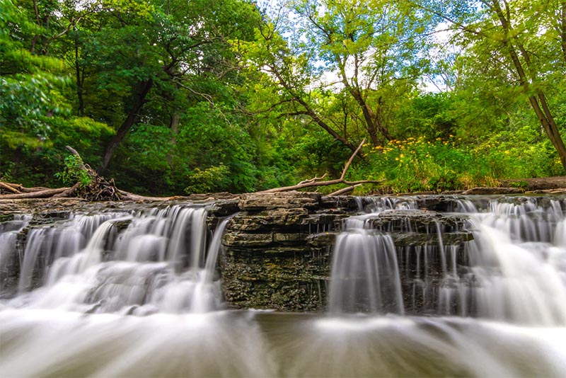 A short, wide waterfall flows over rocks outside Chicago