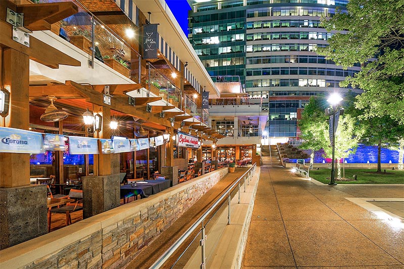 An image at night of a restaurant patio to the left and a business center ahead in The Woodlands