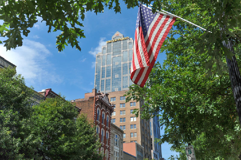 Sunny day looking up at skyscraper with American flag in the foreground.