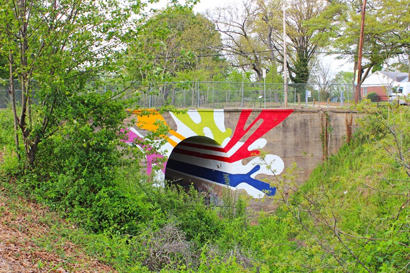 Bridge with bicycle trail and art in covered forest.