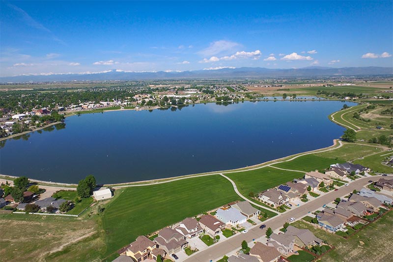 A large lake sits between rows of houses with mountains seen in the very far distance in Denver