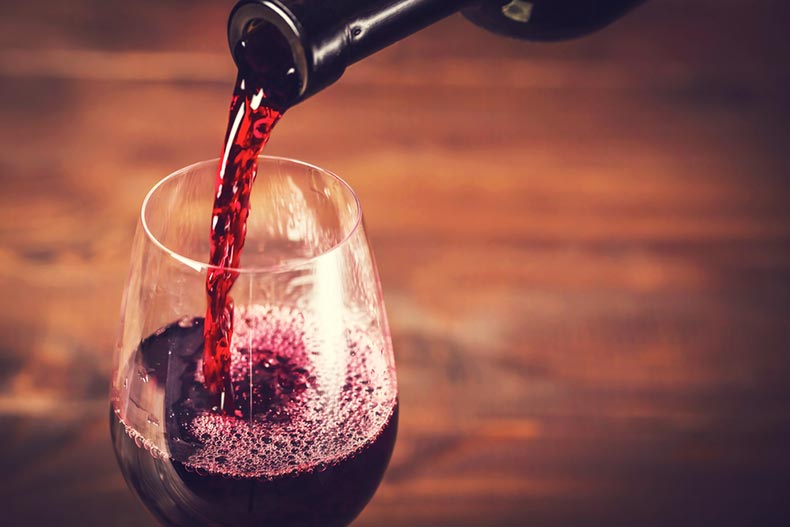 Pouring red wine into the glass against wooden background